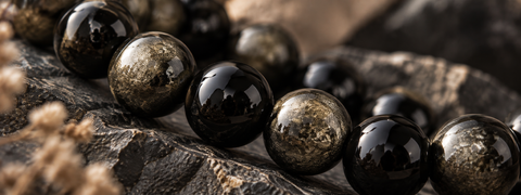 Polierte Obsidian-Natursteinperlen in Schwarz und Goldtönen als Makroaufnahme.