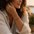 Frau trägt das filigrane African Bloodstone Natursteinarmband mit 6 mm großen Perlen in Grün-, Grau- und Rottönen in einer warmen mediterranen Küstenkulisse.