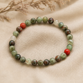 Filigranes African Bloodstone Natursteinarmband mit 6 mm großen Perlen in verschiedenen Grün-, Grau-, Creme- und Rottönen, hochwertig auf hellem Naturstoff inszeniert.
