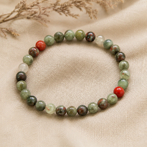 Filigranes African Bloodstone Natursteinarmband mit 6 mm großen Perlen in verschiedenen Grün-, Grau-, Creme- und Rottönen, hochwertig auf hellem Naturstoff inszeniert.