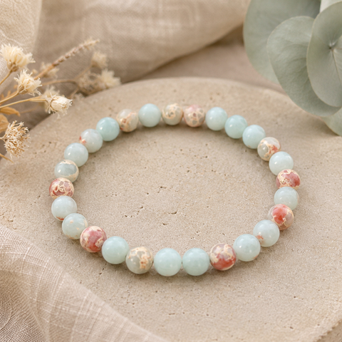 Filigranes Aqua Terra Jasper Natursteinarmband mit 6 mm großen Perlen in Aquablau, Creme, Beige und sanftem Rosé, natürlich auf einer hellen, strukturierten Oberfläche präsentiert.