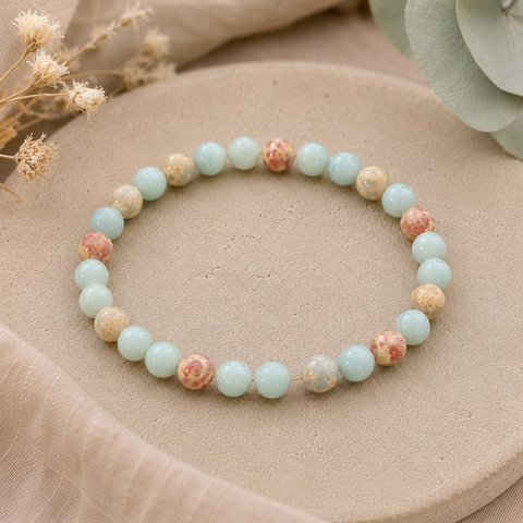 Aqua Terra Jasper Natursteinarmband mit 8 mm großen, individuell gemusterten Perlen in hellem Aquablau, Creme, Beige und Rosé auf einer natürlichen beigen Oberfläche mit dezenten Trockenblumen und Eukalyptus.