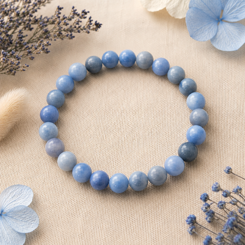 Blue Aventurine Natursteinarmband mit 8 mm großen, natürlich gemusterten Perlen in verschiedenen Blau-, Grau- und Lavendeltönen auf beigefarbenem Stoff mit farblich passenden Naturdetails.