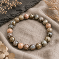 Blue Que Sera Opal Natursteinarmband mit 8 mm großen, polierten Perlen in Blau-, Rosa-, Creme- und grauen Erdtönen, stilvoll auf beigem Leinen mit dunklem Stein und getrockneten Pflanzen inszeniert.