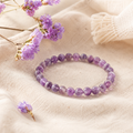 Filigranes Chevron Amethyst Natursteinarmband mit 6 mm großen, violett gemusterten Perlen auf hellem Leinen mit dezent arrangierten lilafarbenen Blüten.