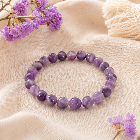 Chevron Amethyst Natursteinarmband mit 8 mm großen, individuell gemusterten Perlen in verschiedenen Violett- und Lilatönen auf hellem Naturstoff mit lilafarbenen Blüten.