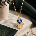 Luxuriöse goldene Hand der Fatima Halskette mit blauem Nazar-Auge und funkelnden Zirkonia-Details auf hellem Naturstein. Elegante Schmuckinszenierung mit dunklen Grüntönen, goldenen Akzenten und orientalischem Ambiente im Stil von AVRE Studios.