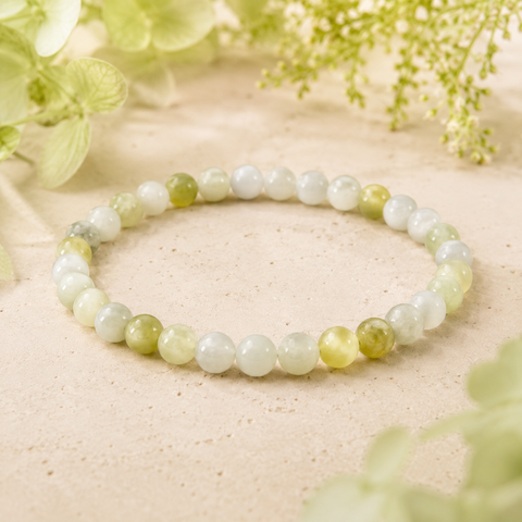 Flower Jade Natursteinarmband mit 6 mm großen, individuell gemusterten Perlen in Weiß, Creme, Hellgrün und Olivgrün auf hellem Naturuntergrund mit zarten grünen Blüten.