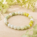 Flower Jade Natursteinarmband mit 8 mm großen, polierten Perlen in Weiß, Creme und verschiedenen Grüntönen, natürlich mit hellgrünen Blumen auf beigem Untergrund präsentiert.