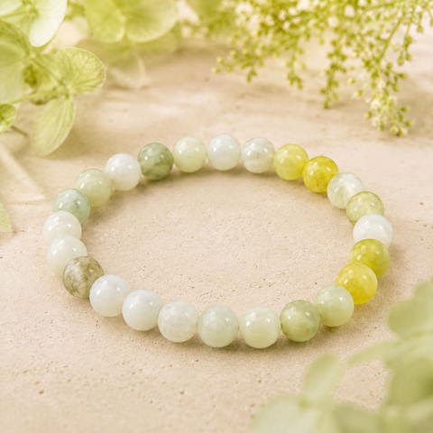 Flower Jade Natursteinarmband mit 8 mm großen, polierten Perlen in Weiß, Creme und verschiedenen Grüntönen, natürlich mit hellgrünen Blumen auf beigem Untergrund präsentiert.