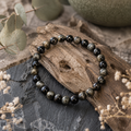 Gold Obsidian Natursteinarmband mit 6 mm großen, schwarz-braunen Perlen und dezent goldfarbenem Schimmer, natürlich auf dunklem Stein und verwittertem Holz inszeniert.