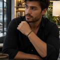 Mann mit schwarzem Hemd trägt das filigrane Gold Obsidian Natursteinarmband mit 6 mm großen dunklen Perlen in einem modernen, warm beleuchteten Café.