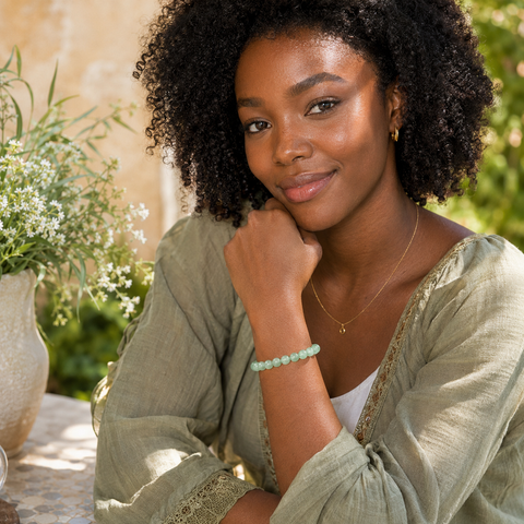 Frau trägt das Green Aventurine Natursteinarmband mit 8 mm großen grünen Perlen zu einem salbeigrünen Oberteil in einer sonnigen, stilvoll bepflanzten Gartenumgebung.