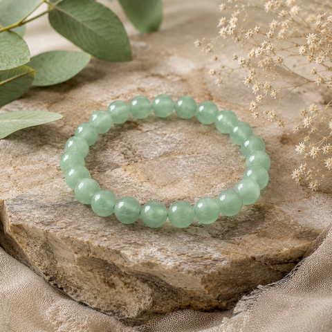 Green Aventurine Natursteinarmband mit 8 mm großen, polierten Perlen in einem sanften Grünton auf einer natürlich strukturierten Steinfläche mit Eukalyptus und hellen Blüten.