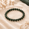 Green Sandstone Natursteinarmband mit 8 mm großen, glänzenden dunkelgrünen Perlen auf beigefarbenem Leinen, ergänzt durch Trockenblumen und einen dezenten dunkelgrünen Stoffakzent.