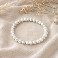 Filigranes Howlite Natursteinarmband mit 6 mm großen, mattierten Perlen in Weiß mit feiner grauer Marmorierung, natürlich auf hellem Leinenstoff präsentiert.