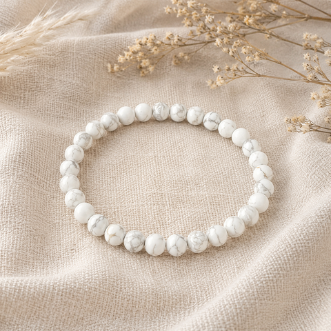 Filigranes Howlite Natursteinarmband mit 6 mm großen, mattierten Perlen in Weiß mit feiner grauer Marmorierung, natürlich auf hellem Leinenstoff präsentiert.