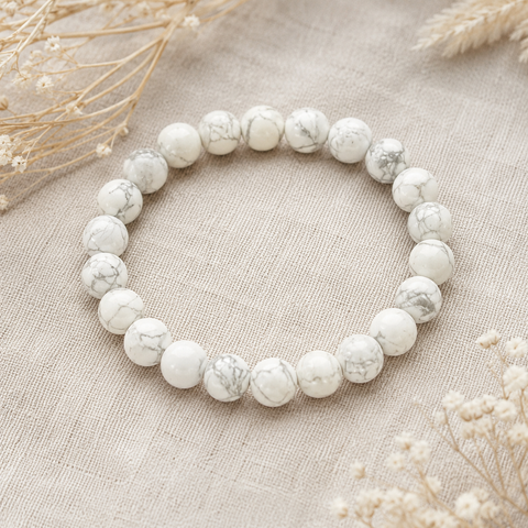 Howlite Natursteinarmband mit 8 mm großen, mattierten weißen Perlen und dezenter grauer Marmorierung, stilvoll auf einem hellen Naturstoff inszeniert.