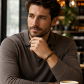 Mann mit dunkelbraunem Poloshirt trägt das Iron Tiger Eye Natursteinarmband mit 8 mm großen, braun-golden gemusterten Perlen in einem modern und warm beleuchteten Café.