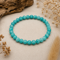 Lake Blue Jade Armband mit 6 mm großen, gefärbten Perlen in kräftigem Türkisblau auf hellem Leinen mit beigefarbenen Trockenblumen und natürlichen Dekoelementen.