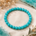 Lake Blue Jade Armband mit 8 mm großen, leicht marmorierten und gefärbten Perlen in Türkisblau auf hellem Naturstoff mit dezenten Blumen und farblich passenden Akzenten.
