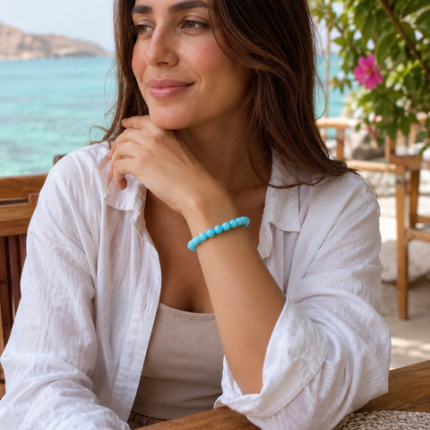 Frau trägt das Lake Blue Jade Armband mit 8 mm großen türkisblauen Perlen am Handgelenk in einer hellen, natürlichen Küstenkulisse mit Blick auf das Meer.