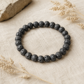 Schwarzes Lavastein-Armband mit 8 mm großen, porösen Perlen auf hellem Leinen, umgeben von dezenten Trockenblumen und natürlichen Beigetönen.