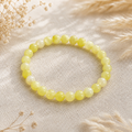 Filigranes Lemon Jade Natursteinarmband mit 6 mm großen, leicht transparenten Perlen in Zitronengelb und Creme auf hellem Leinen mit natürlichen Trockenblumen.