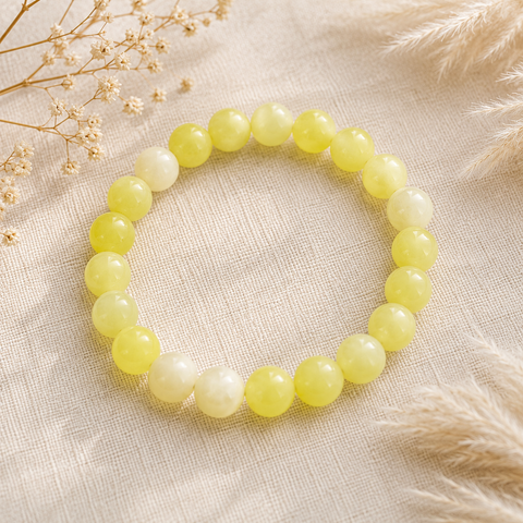 Lemon Jade Natursteinarmband mit 8 mm großen, polierten Perlen in kräftigem Zitronengelb und hellen Cremetönen auf beigefarbenem Naturstoff mit getrockneten Gräsern.