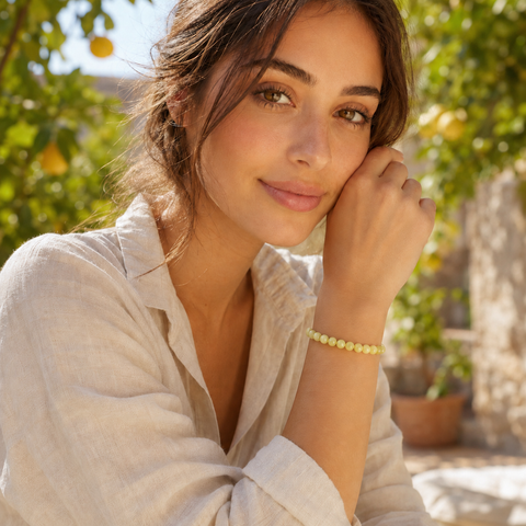 Frau trägt das Lemon Jade Natursteinarmband mit 8 mm großen gelben und cremefarbenen Perlen am Handgelenk in einer sonnigen, natürlichen Gartenkulisse mit Zitronenbaum.