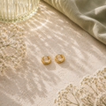 Kleine goldfarbene Luna Creolen in 8 mm Größe auf hellem Naturstein mit Glasvase, sanften Lichtreflexen und feinen weißen Blüten im eleganten AVRE Studios Stil.