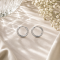 Luna Creolen in Silber mit 12 mm Durchmesser aus hochwertigem Edelstahl. Zeitlose Mini-Creolen mit glänzender Oberfläche, stilvoll präsentiert auf hellem Stoff mit feinen Lichtreflexionen, Glasstruktur und weißen Blüten für einen eleganten und modernen Look.