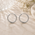 Luna Creolen in Silber mit 16 mm Durchmesser aus hochwertigem Edelstahl. Zeitlose mittelgroße Creolen mit glänzender Oberfläche, stilvoll inszeniert auf heller Natursteinoptik mit sanften Lichtreflexionen, Glasstruktur und feinen weißen Blüten im Hintergrund.