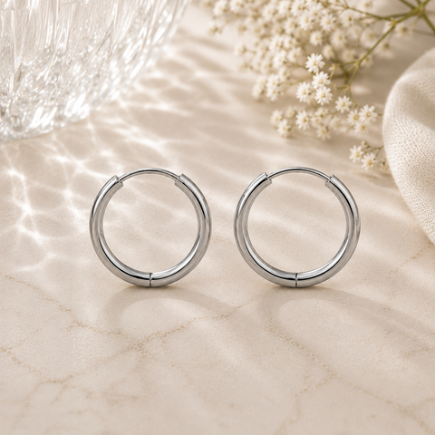 Luna Creolen in Silber mit 16 mm Durchmesser aus hochwertigem Edelstahl. Zeitlose mittelgroße Creolen mit glänzender Oberfläche, stilvoll inszeniert auf heller Natursteinoptik mit sanften Lichtreflexionen, Glasstruktur und feinen weißen Blüten im Hintergrund.