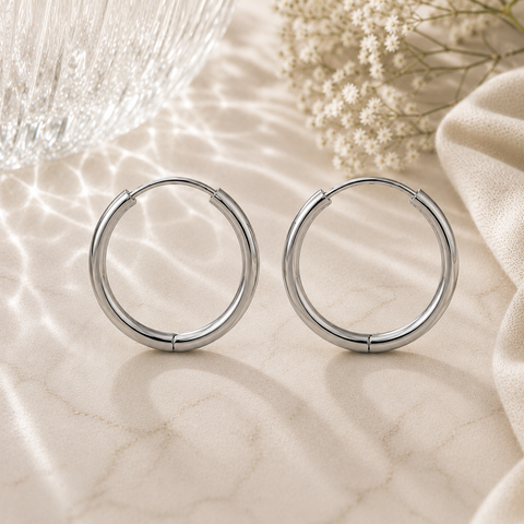 Luna Creolen in Silber mit 18 mm Durchmesser aus hochwertigem Edelstahl. Elegante mittelgroße Creolen mit glänzender Oberfläche, präsentiert auf heller Natursteinoptik mit feinen Lichtreflexionen, Glasstruktur, weißen Blüten und weichem Stoff im Hintergrund. Ideal für einen zeitlosen und modernen Look.