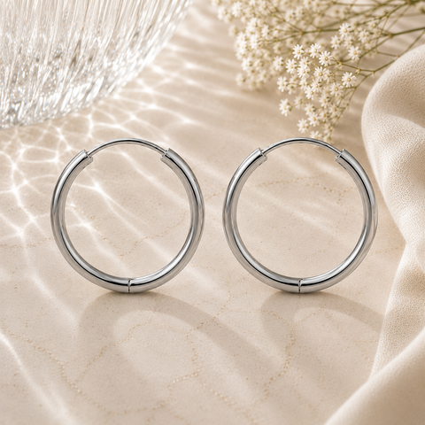 Luna Creolen in Silber mit 20 mm Durchmesser aus hochwertigem Edelstahl. Klassische große Creolen mit glänzender Oberfläche, stilvoll inszeniert auf heller Natursteinoptik mit sanften Lichtreflexionen, Glasstruktur, weißen Blüten und elegantem Stoff im Hintergrund. Zeitloser Ohrschmuck für Alltag und besondere Anlässe.
