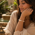 Brünette Frau trägt das Marokko Jade Armband mit 8 mm großen, hellen Natursteinperlen in Cremeweiß, Beige und zarten Rosétönen in einem sonnigen orientalischen Innenhof.