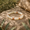 Marokko Jade Armband mit 8 mm großen, cremeweißen und sanft beigefarbenen Natursteinperlen, stilvoll in einer warmen, natürlichen Umgebung mit dezenten grünen Akzenten präsentiert.