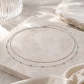 Elegante silberfarbene doppellagige Bauchkette mit filigranen Kugeldetails auf hellem Travertinstein inszeniert. Minimalistischer Damenschmuck von AVRE Studios für moderne Sommer-, Urlaubs- und Alltagslooks.
