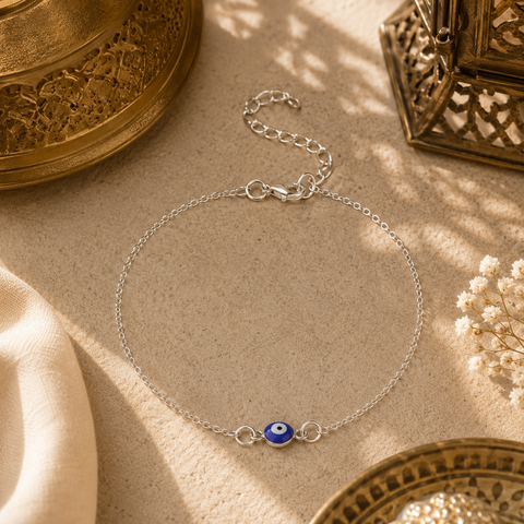 Filigrane silberfarbene Nazar Fußkette mit blauem Auge als orientalischem Schutzsymbol. Stilvoll inszeniert auf hellem Naturstein mit traditionellen Ornamenten, feinem Stoff, zarten Blüten und warmem Sonnenlicht. Eleganter Sommerschmuck mit mediterran-orientalischer Ausstrahlung für Alltag und besondere Anlässe.