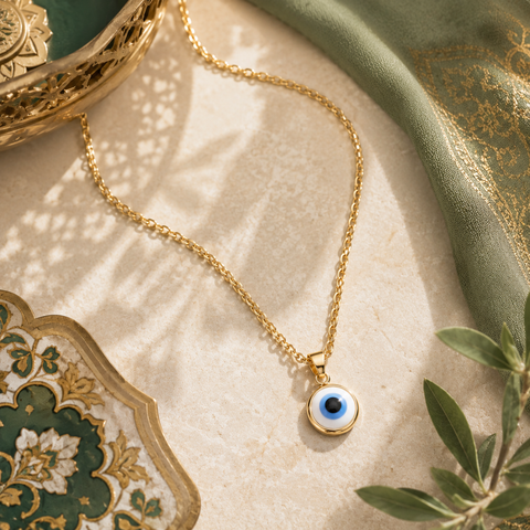 Goldene Nazar Halskette mit weiß-blauem Nazar Auge Anhänger auf elegantem beigen Naturstein mit orientalischen grünen und goldenen Dekoelementen im luxuriösen AVRE Studios Stil.