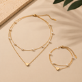 Schmuckset mit Herzanhänger und feinen weißen Perlen bestehend aus Layer-Halskette und passendem Armband auf beigem Hintergrund mit warmem Licht und natürlichen Schatten.