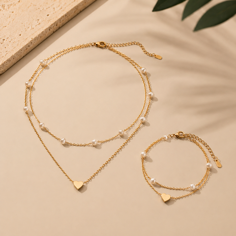 Schmuckset mit Herzanhänger und feinen weißen Perlen bestehend aus Layer-Halskette und passendem Armband auf beigem Hintergrund mit warmem Licht und natürlichen Schatten.