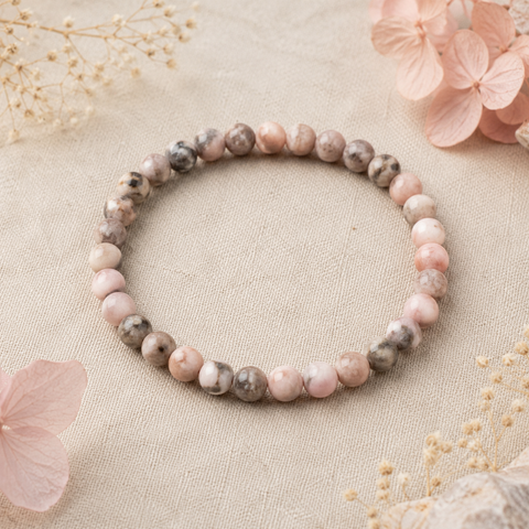 Pink Zebra Jasper Natursteinarmband mit 6 mm großen, individuell gemusterten Perlen in Rosa, Taupe, Grau und Creme auf hellem Leinen mit dezenten Trockenblumen.