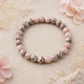 Pink Zebra Jasper Natursteinarmband mit 8 mm großen, marmorierten Perlen in Rosa, Beige, Grau und Braun auf beigefarbenem Naturstoff mit zarten floralen Akzenten.