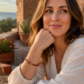 Frau trägt das Red Jasper Natursteinarmband mit 6 mm großen, matt wirkenden Perlen in warmen Rot-, Braun- und Beigetönen in einer sonnigen mediterranen Umgebung.