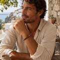 Mann trägt das Red Tiger Eye Natursteinarmband mit 8 mm großen rotbraunen Perlen am Handgelenk in einer warmen mediterranen Umgebung.