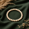 Filigranes Riverstone Natursteinarmband mit 6 mm großen, runden Perlen in sanften Creme- und Beigetönen auf dunkelgrünem Stoff stilvoll präsentiert.