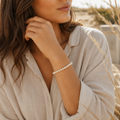 Frau trägt das filigrane Riverstone Natursteinarmband mit 6 mm großen Perlen in sanften Beige- und Cremetönen in einer natürlichen, hellen Umgebung am Handgelenk.
