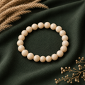 Riverstone Natursteinarmband mit 8 mm großen, glatten Perlen in hellen Creme-, Sand- und Beigetönen auf dunkelgrünem Stoff dekorativ inszeniert.
